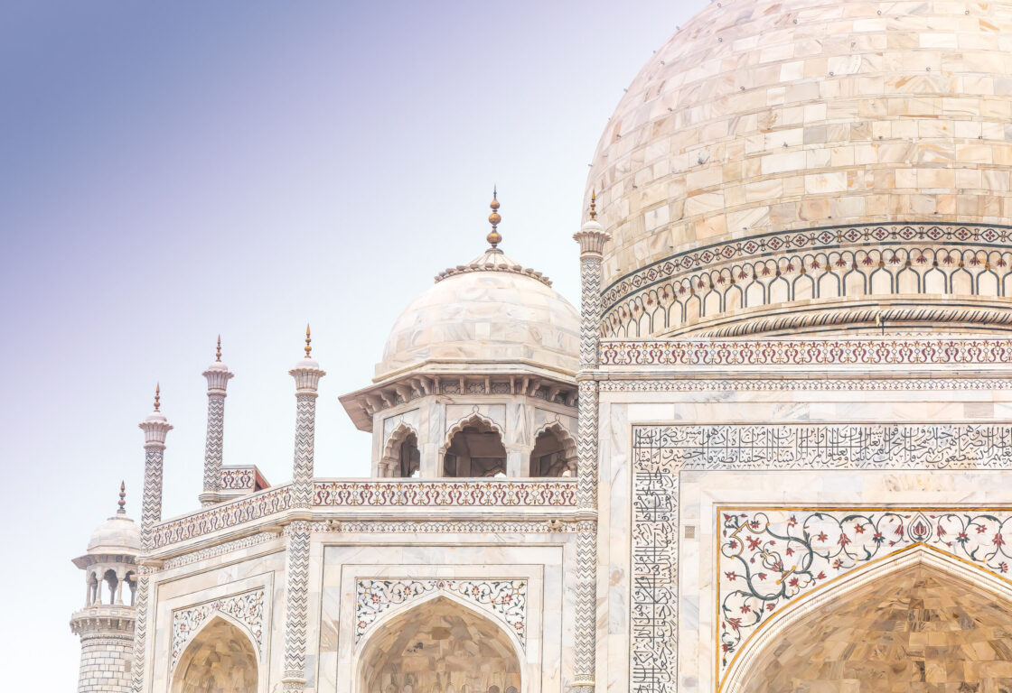 Ornate top corner of the Taj Mahal, showing the white marble dome and intricate finial against a clear sky showing the intricate designs in india