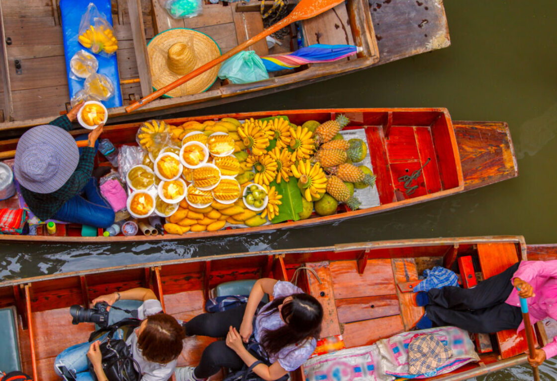 view above three boats next to each other and the middle boat has a variety of yellow coloured fruits and one boat has three people in with cameras and the other boat has a hat and some fruit on and the water is flat and calm underneath