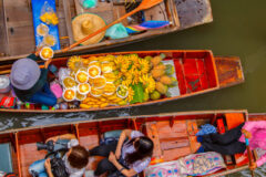 view above three boats next to each other and the middle boat has a variety of yellow coloured fruits and one boat has three people in with cameras and the other boat has a hat and some fruit on and the water is flat and calm underneath