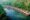 a line of huts that sit on floating platforms runs along the edge of a hill and they sit on a calm river that has one small boat travelling down