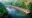 a boat travels down a river and on the right hand side is a row of thatched huts with seating areas floating on the river