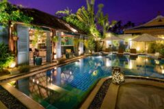 maison vy outdoor pool at nightime with bar or restaurant on the left hand side with open shutters onto the pool