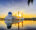 stunning white mosque with main copula and two towers located on water with a mirror like reflection and sunset setting behind it