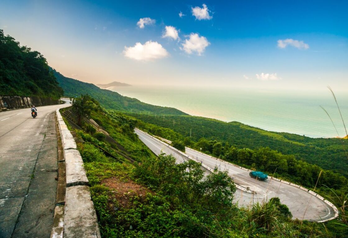 bending roads of the hai van pass in vietnam with cars going down and stunning views surrounding and sea in the distance