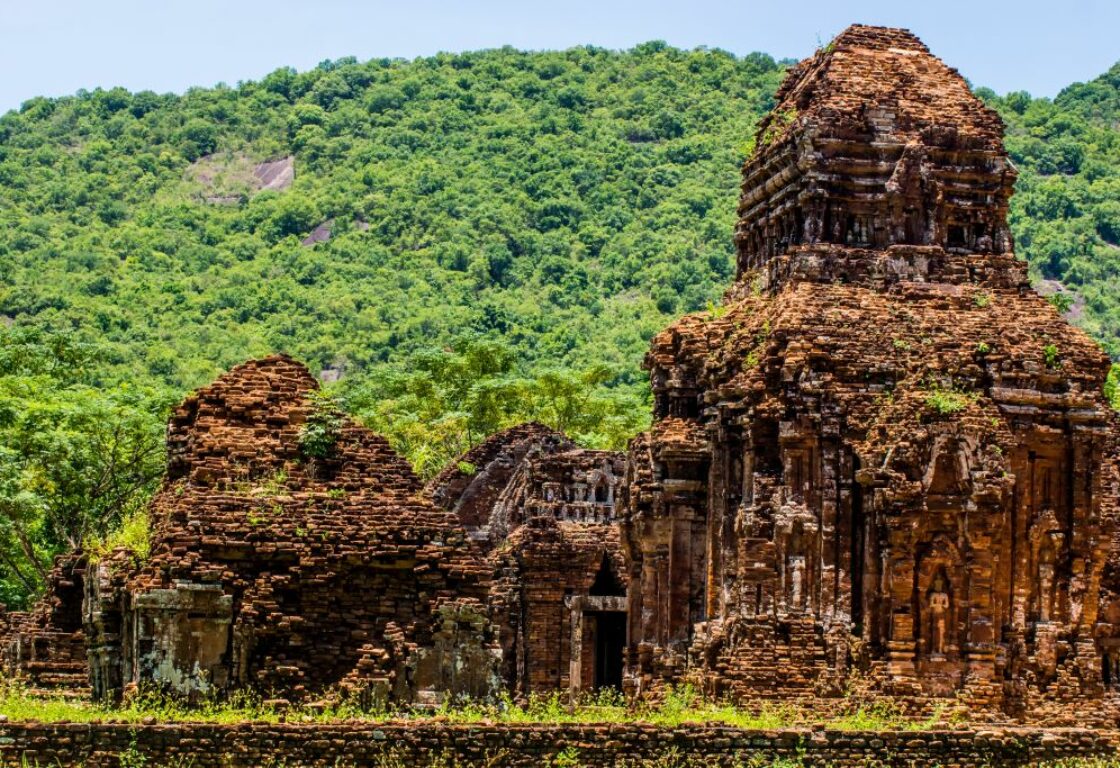 old temple ruins in front of a green hill with red brick