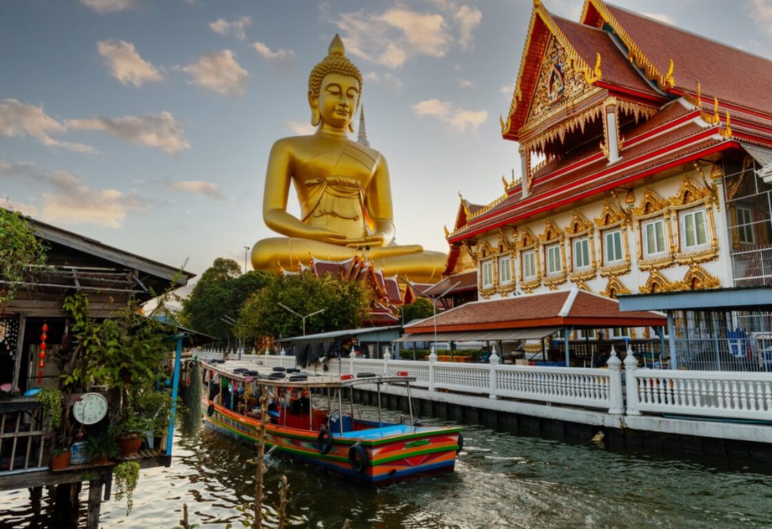 Big Buddha Dhammakaya Tep Mongkol Buddha of Paknam Bhasicharoen temple in Thonburi in Bangkok city against the backdrop of sunset and canal