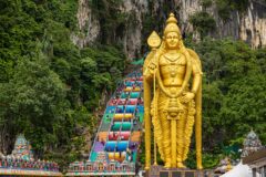 gold statue in fron of famous Batu Caves with colorful stairs in Kuala Lumpur