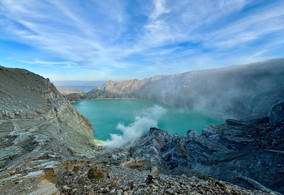 crater on mount ijen in indonesia is full with turquoise blue water whilst grey stone rises up from the water to form the crater