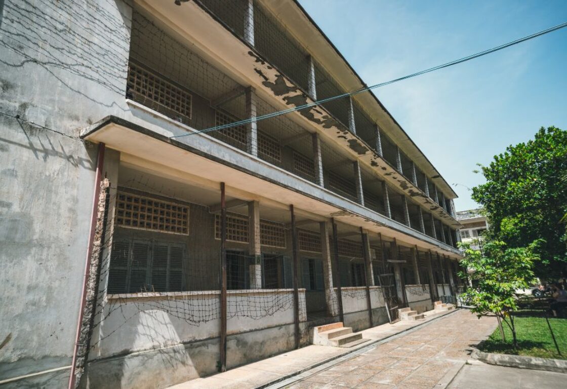 picture of outside an old school building with barbed wire across the front taken from the courtyard in phnom penh, cambodia and a small patch of grass sits opposite