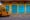 a yellow wall with four large bright blue doors with carvings in and on the left the front of a yellow rickshaw in delhi is parked by the side of the road