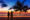 a man and a woman hold hands on the beach with a palm tree next to them looking out to sea with the sky turning shades of blue and pinks to watch the sunset