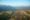 birds eye view of vang vieng with hot air balloon flying over a river with the roofs of many houses underneath and mountains in the distance
