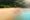 a quiet stretch of white sand beach taken from above and two small people walk along the sand and one side of the sand is framed by thick forest and on the other side is flat sea the colour of turquoise