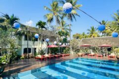 blue pool with blue lanterns hanging above the water at villa maly and a large wooden deck surrounds the pool with bright sun loungers on and a two level building stands overlooking the view with windows that have green shutters
