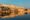 yellow sandstone fortress on a hillside, reflected in the water of a lake below