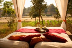Luxury outdoor daybed at a heritage hotel in rural India, overlooking farmland and forest, with white drapes, colourful cushions and sunset drinks creating a relaxing countryside retreat.