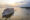 white ship with three levels and a pointed tip cruising along a wide river as the sun sets turning the water shades of pink and blue