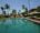 Knai Bang Chatt in cambodia pool with palm trees at the end of the pool and a wooden decking with sun loungers and umbrellas