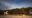 Komodo Resort in indonesia a long hut with a bamboo roof and tables and chairs sits on the sand with a hill behind and next to the large bamboo hut are other smaller huts partially hidden