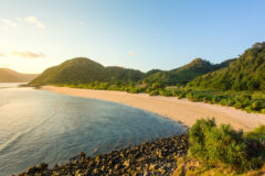 a long beach on lombok in bali with greenery and a hill growing behind the white sand