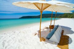 pristine white sand with towels and cushions under umbrellas and with clear sea rolling out in front