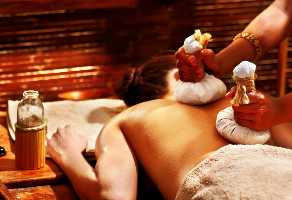 a woman lying on her front receiving a massage with two packages wrapped in linen