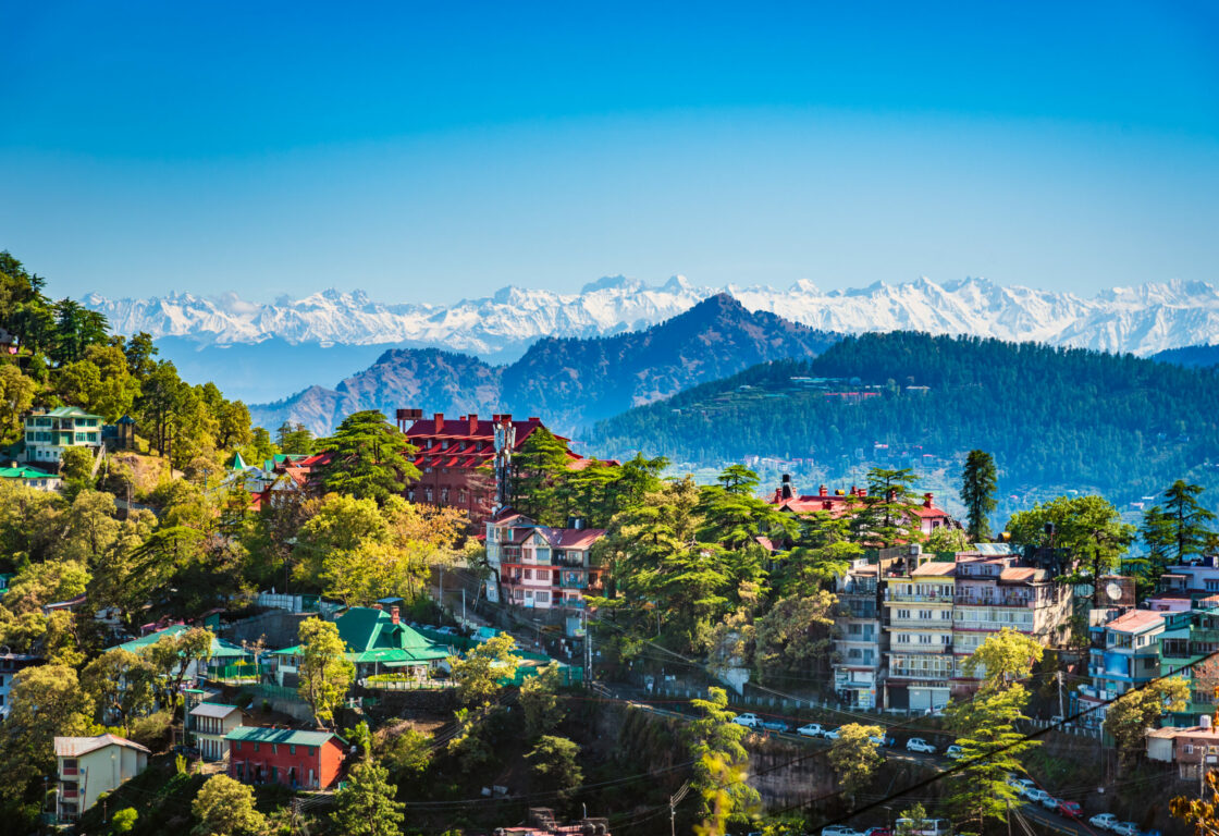 Himachal Pradesh in india a mountain town with long houses on the edge with mountains topped with snow in the background