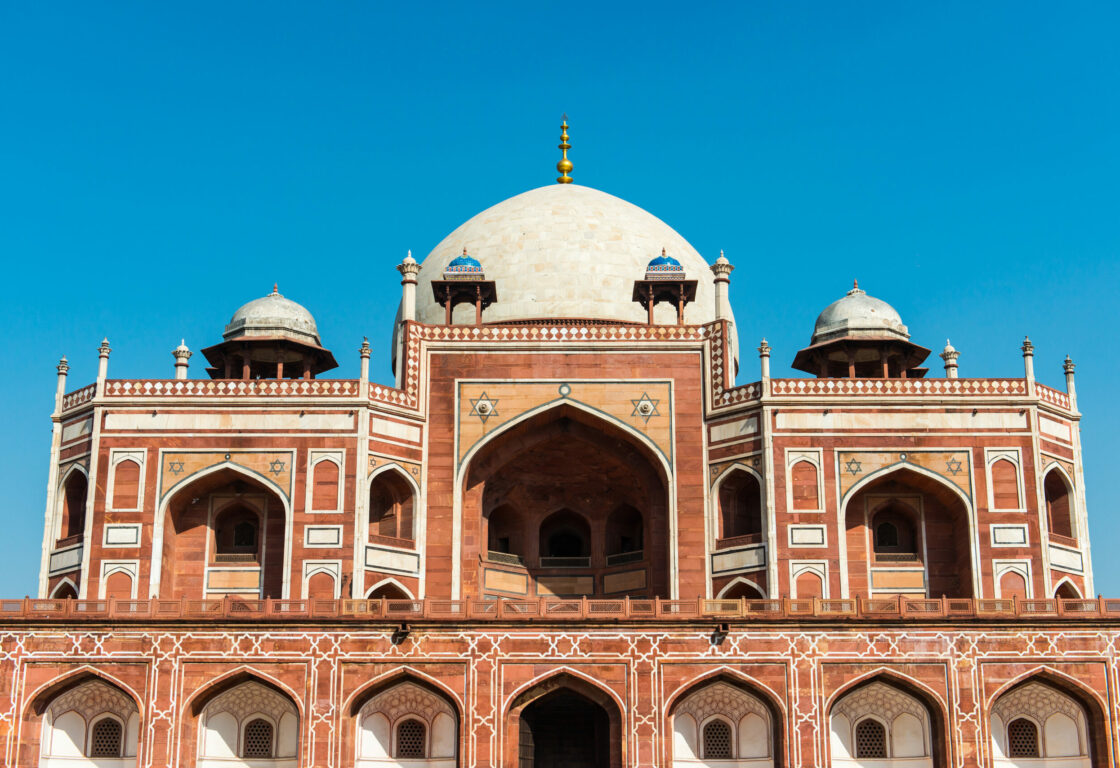 mausoleum featuring intricate red sandstone and white marble architecture, with a large central dome surrounded by beautifully landscaped gardens and symmetrical pathways under a clear blue sky in india
