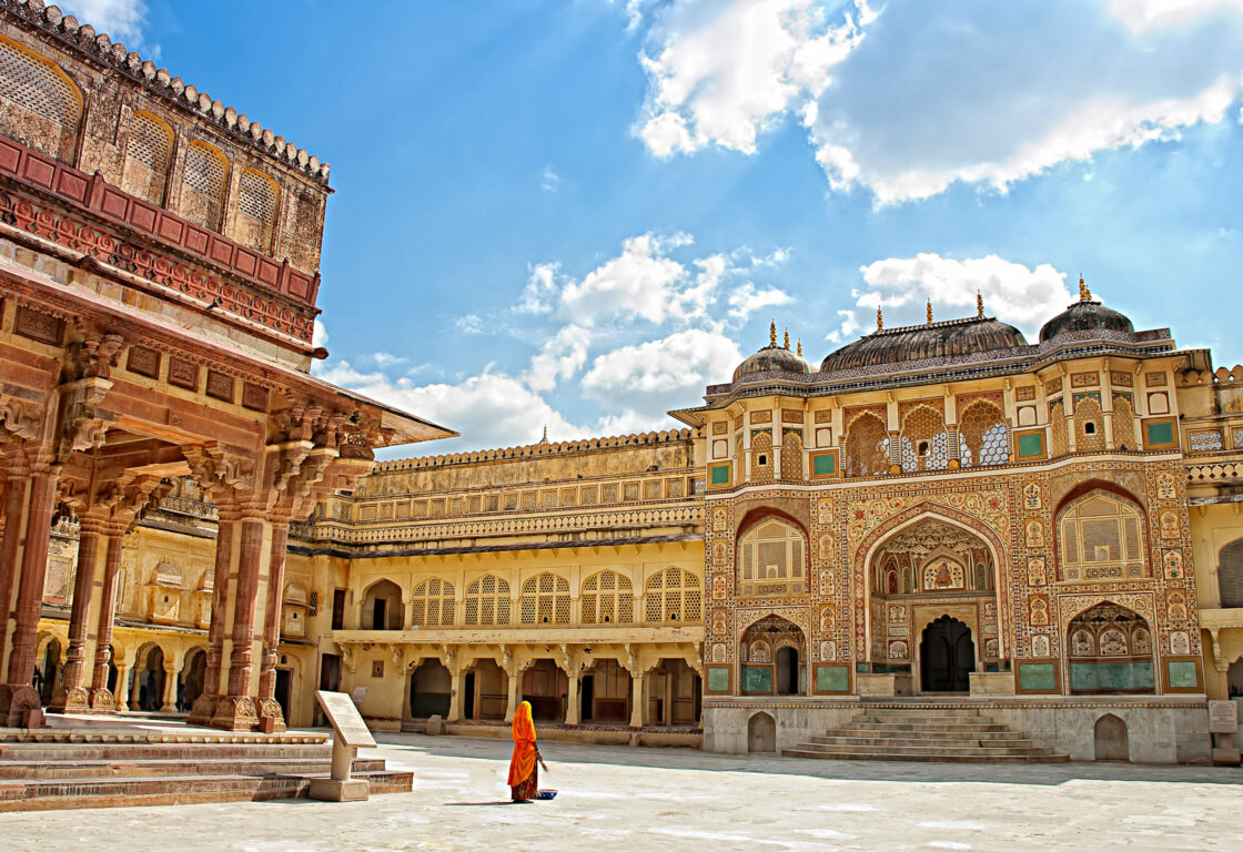woman stands in the amber fort in Jaipur, Rajasthan, in front of a detailed gateway designed with mosiacs and detail in india