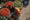 aerial view of a market in rajasthan in india where an old woman with her head covered in a yellow scarf leans over large baskets filled with tomatoes and green beans