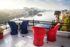two tables with chairs on a roof terrace over looking a river in udaipur india, and buildings lining each side of the river
