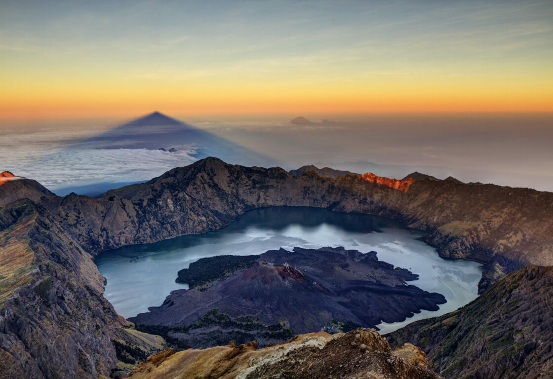 Mount Rinjani crater with a lake and a piece of land in the centre of the crater and clouds surrounding the crater