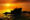Silhouette of Tanah Lot temple on a large rock with a golden sunset and people walking along the shore