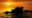 Silhouette of Tanah Lot temple on a large rock with a golden sunset and people walking along the shore