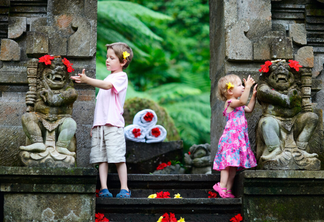 a boy and a girl stand on either sides of some steps touching monkey statues next to them with yellow flowers in their hair and red flowers on the steps and statues