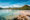 a pale pink beach with clear sea and a tourist boat in the distance sits underneath a line of green hills