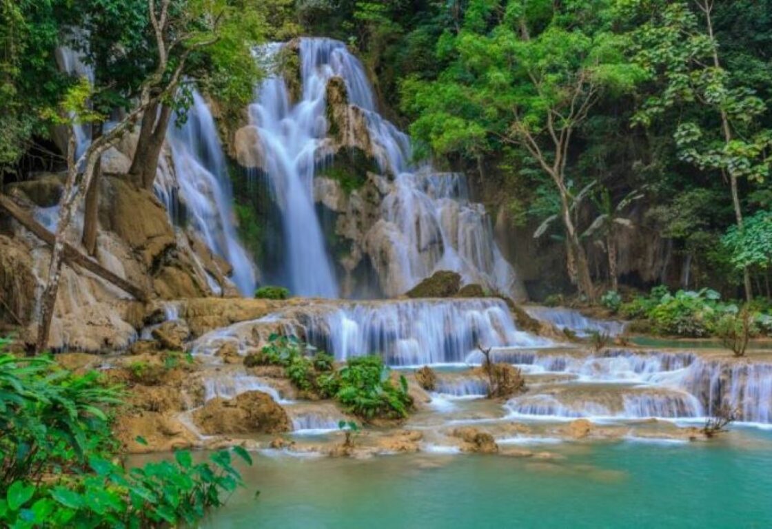 a giant cascade of water goes into a pool at the bottom that has tiered sections and green trees frame either side of the falling water