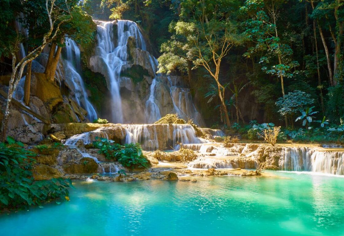 the kuang si waterfalls cascading down through tropical jungle, into a large turquoise blue pool at the bottom in laos
