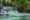 kuang si waterfalls in luang prabang, laos, with one tall level rushing water into a pool of turquoise blue water below that has a couple of different levels and trees surround the whole area