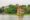 Hoan Kiem Lake in Vietnam is a flat body of water and on the far side a line of trees and on the water a patch of grass has a small monument that has little arches all the way around the outside