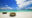 circular boats sit on bright white sand and in the background a turquoise sea is flat and calm and above a blue and cloudy sky