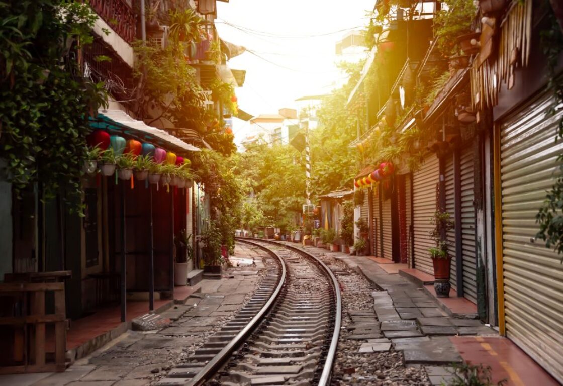 sunsetting through hanoi train street with train tracks running down the centre of the street and on either side are shops with shutters drawn