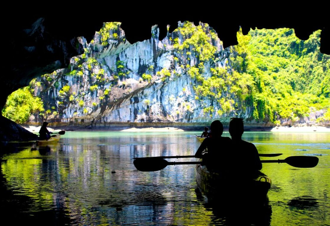 silhouettes of people kayaking through a cave in ha long bay and the dark cave opens on to a bright area lit up by the sun