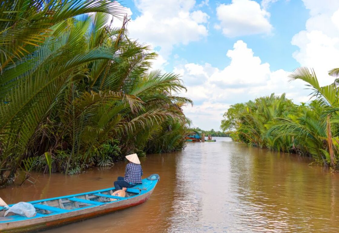 fisherman on a quiet part of the mekong delta in vietnam floating down the river with no one else around in a long blue boat