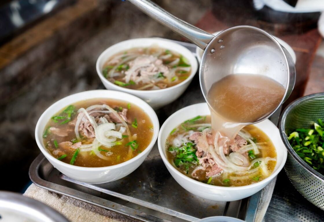 three bowls of noodle soup with liquid being poured into one bowl and ingredients such as noodles and herbs in the middle of the bowls