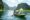 Tourists on a traditional wooden boat being rowed through Tam Coc, Vietnam, with dramatic limestone karst mountains rising from lush green vegetation on both sides of the calm river waterway. A local rower wearing a conical hat steers the boat