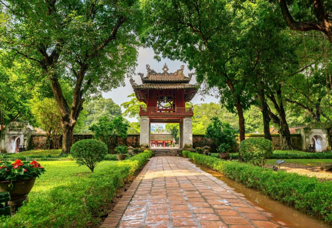 temple in gardens at the temple of literature in hanoi in vietnam with a path going down the centre of the image leading to a small pagoda style building and trees and gardens line the path