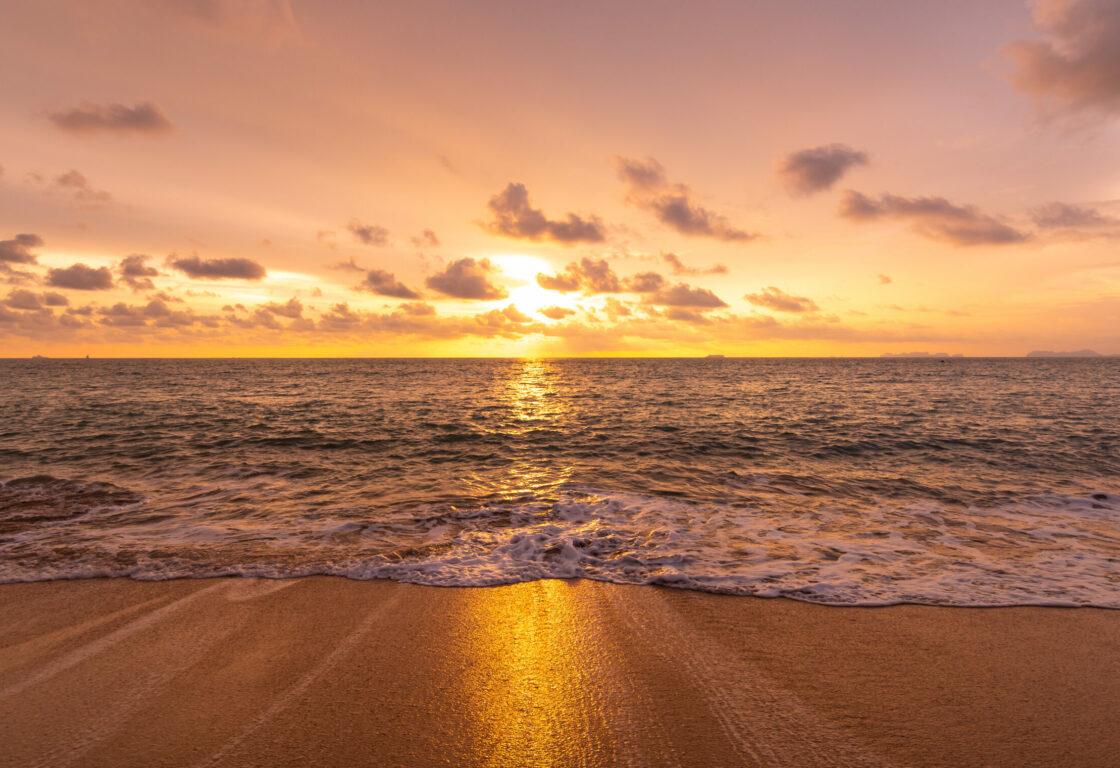 a stretch of golden sand with the sea rolling onto it and a golden sunset casts a golden reflection on to the water in the middle of the picture