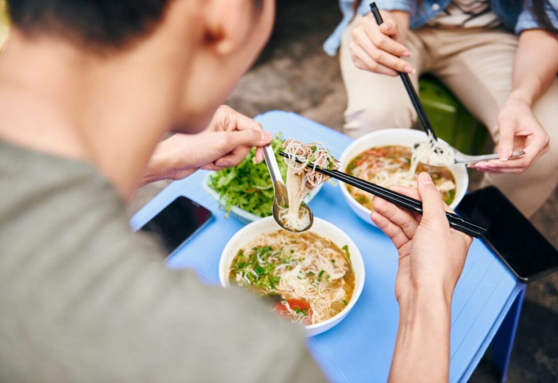 looking over someone's shoulder with a bowl of noodles on the table
