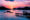 a flat sea as the sun sets creating a beautiful pink and purple sky and the sihlouettes of boats and small hills against the sky and a pier goes out over the sea